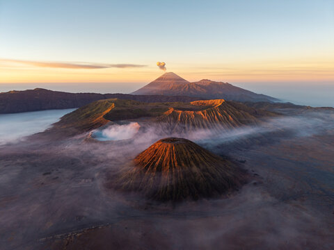 Majestic volcanoes rise above misty valleys at dawn. Soft light bathes rugged peaks in golden hues at Bromo