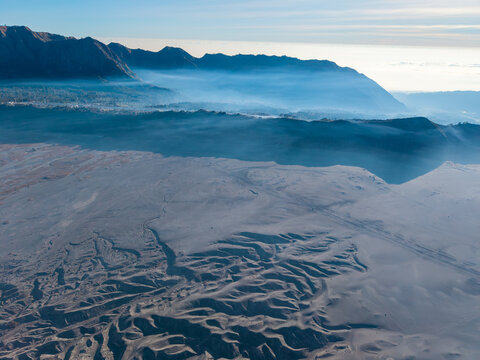 Mountain ridges, layered clouds, volcanic terrain, and distant settlements create a sweeping daytime panorama from Bromo Hill.