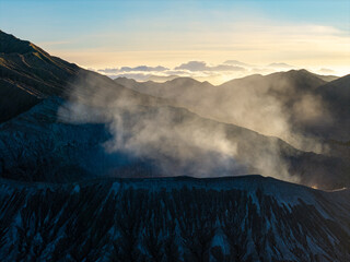 Misty dawn blankets rugged mountain ridgelines. Soft light spills over distant peaks in golden hues at Bromo Crater © Cloudyew