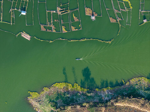 A serene aerial view of a green water body featuring a small boat and fish farms at Waduk Karangkates