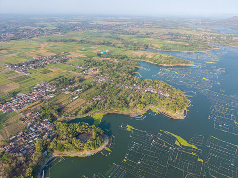 Drone panorama shows Waduk Karangkates reservoir, extensive farmland, rural settlements, wooded shoreline, and floating aquaculture cages.