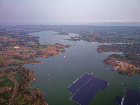 Aerial view of floating solar panels across Bendungan Karangkates reservoir, surrounded by farmland, villages, shorelines, and distant hills.