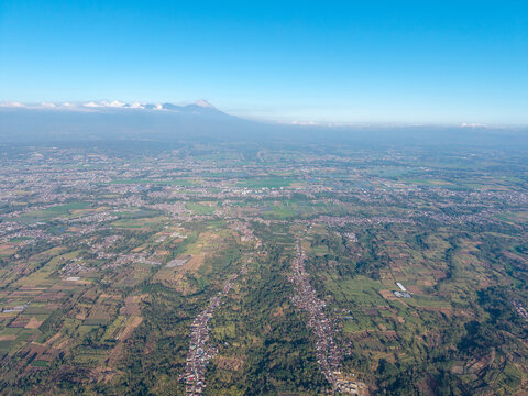 Stunning aerial shot showcasing a vast landscape beneath a clear blue sky, with a majestic mountain in the background at rural Malang