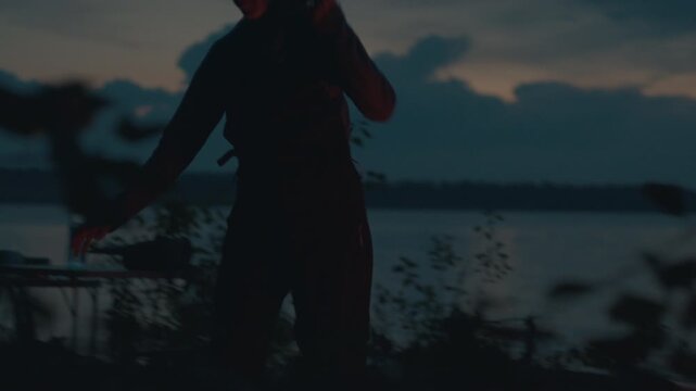 Sailing and camping in the wild. Woman sailor walks on the wild area with sailing boat on the background and bonfire on the foreground