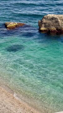 sea and rocks,Clear turquoise water and coastal rocks by a pebble beach, gentle waves,vertival video
