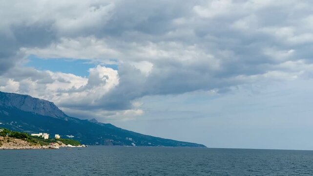 Timelapse: fast-moving clouds over mountain coastline and open sea, wide shot