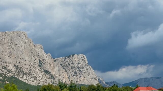 Wide landscape of light‑gray rocky mountains and ridge on the horizon. Dense dark‑blue storm clouds loom above, with lighter patches in the sky