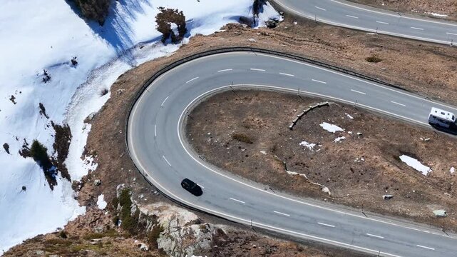 hairpin bend curves sharply white camper van black car round tight turn guardrail dry slope snow patches julier pass alpine route graubunden switzerland high altitude crossing