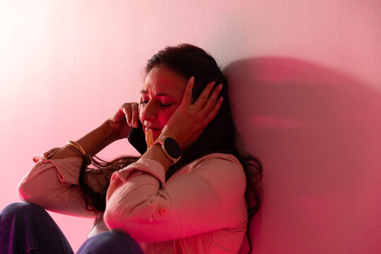 Woman sitting on floor against pale wall, holding smartphone to ear, showing smartwatch, bracelets