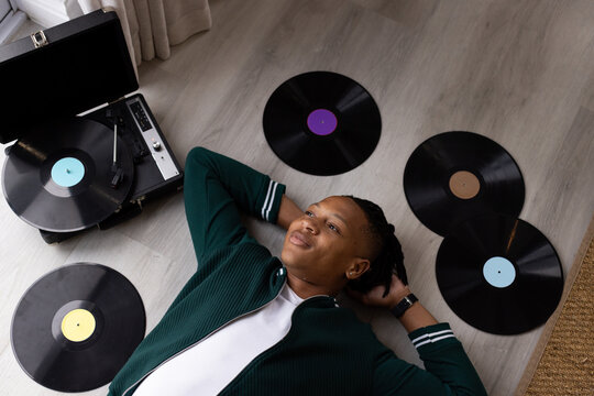 African American male lying on floor at home wearing dark green jacket, turntable playing vinyl