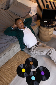 African man in his 20s reclining on bedroom floor beside low bed, turntable playing vinyl records