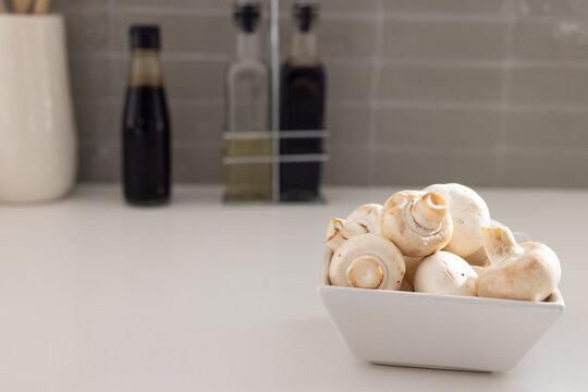 White ceramic bowl is holding button mushrooms on counter near gray tile and bottles, copy space