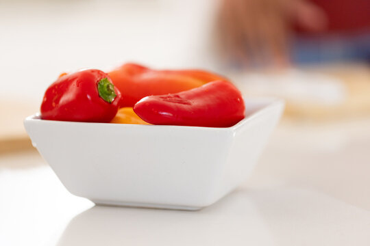 White ceramic bowl is sitting on glossy countertop while red and orange peppers are glistening