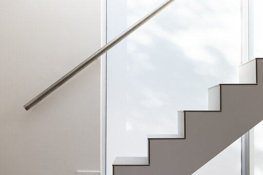 Geometric straight staircase rising to right in modern stairwell with stainless rail, frosted glass