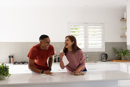 African American couple laughing and cleaning kitchen island in modern kitchen with spray bottle