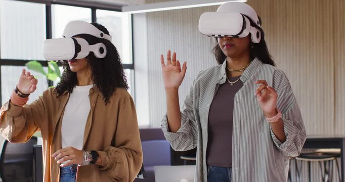 Diverse coworkers wearing white VR headsets, following VR prompt and making hand gestures at office