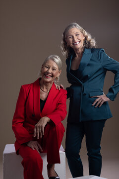 Senior female friends posing together in studio wearing red and teal suits with cube