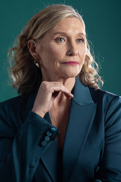 Senior woman posing in portrait studio wearing teal blazer, holding chin and gazing right with ring
