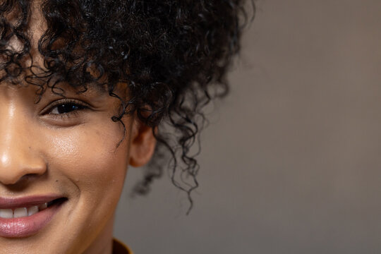 African woman smiling softly while showing tight curly hair and mustard collar in studio