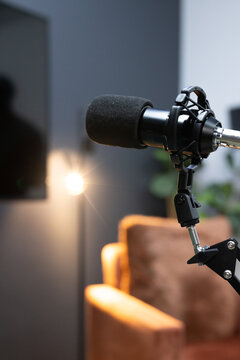 Black broadcast microphone is occupying right foreground on boom arm in home studio, lamp flare
