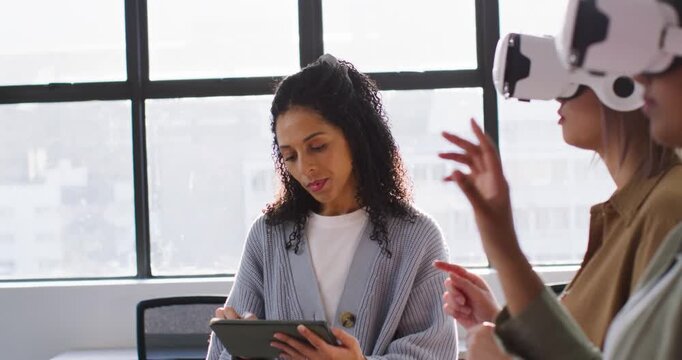 Women demoing in office after white VR headset start center woman tapping tablet overseeing peers