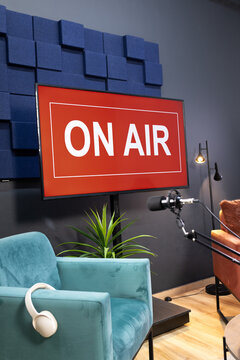 Flat-screen monitor is displaying ON AIR sign in podcast studio, with boom microphone nearby