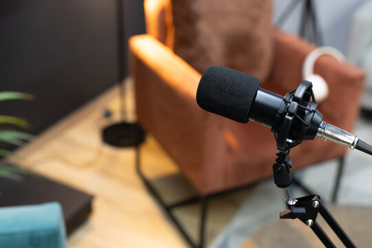 Black broadcast microphone is sitting on boom arm in cozy recording corner, cables visible