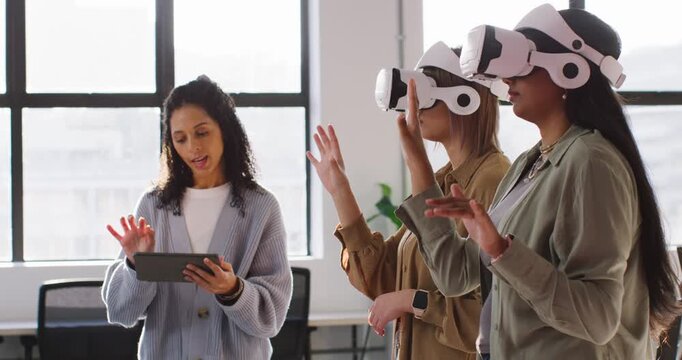 Diverse female trainer tapping tablet in office training two women with VR into precise tapping