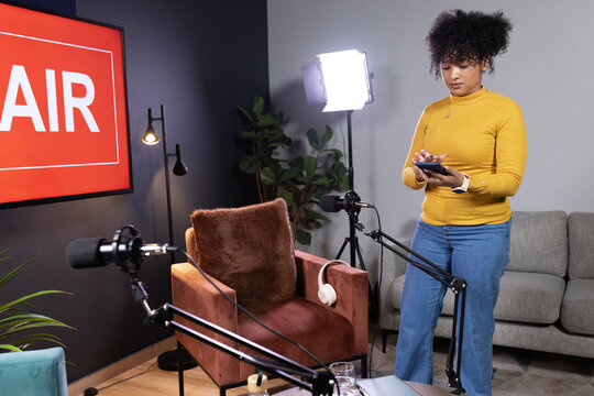 African American woman checking phone on right inside studio near mics and AIR display, copy space