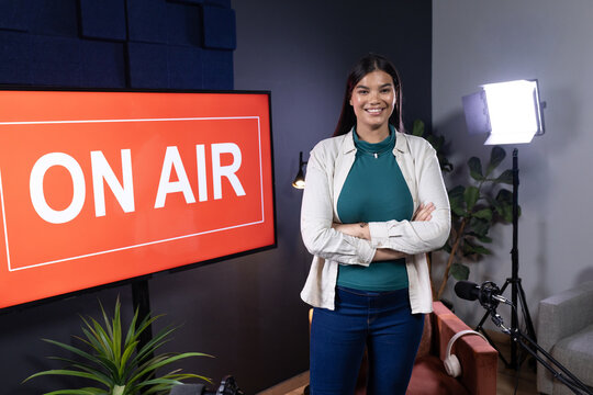Adult female host standing right of monitor showing ON AIR, crossing arms, mic boom and headphones
