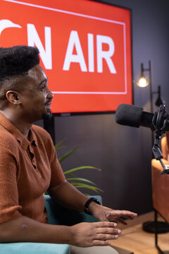 African American man speaking into broadcast mic in podcast studio, gesturing toward ON AIR sign