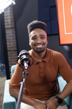 African American man sitting in teal armchair in recording studio, speaking into condenser mic