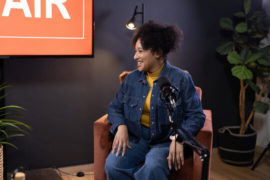 African American woman wearing denim jacket speaking into microphone in studio with AIR panel