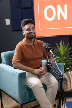 African American adult male sitting at recording studio in teal armchair, speaking into mic