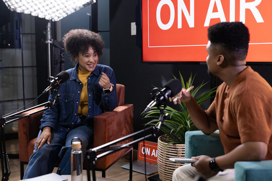 African American podcast co-hosts in denim and rust, speaking into mics in studio with ON-AIR sign