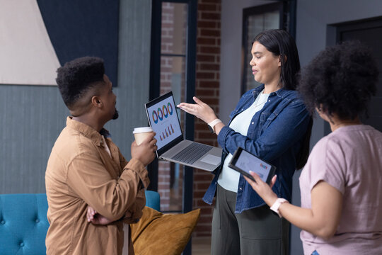 African American coworkers presenting laptop charts while consulting tablet in modern office lounge