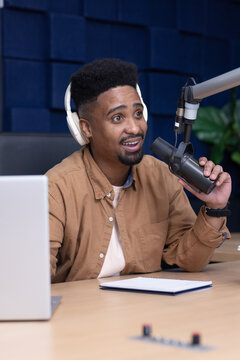 Adult African American man wearing white headset and brown shirt holding mic in studio speaking