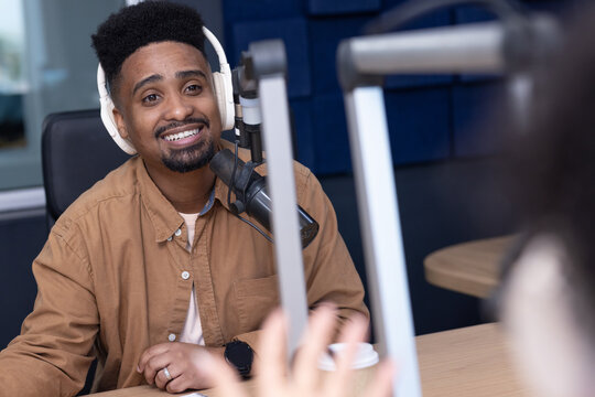 African American man hosting and speaking into broadcast mic wearing headphones at studio table