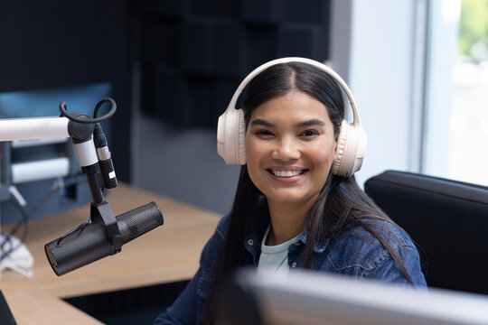 African American woman recording podcast in studio wearing white headphones and speaking into mic