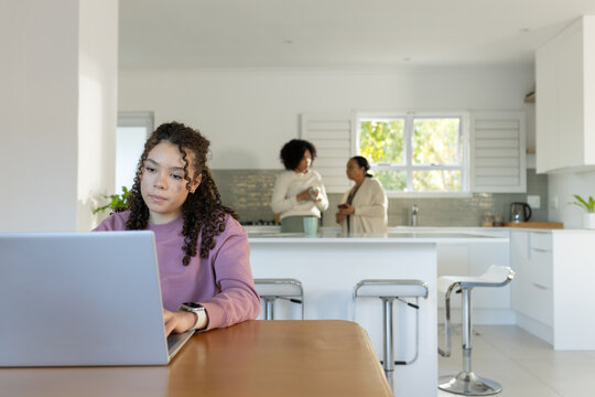 African American female family talking in kitchen; youth in mauve sweater using laptop, copy space