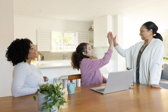 African American family, teenage daughter giving highfive to senior woman in kitchen with laptop