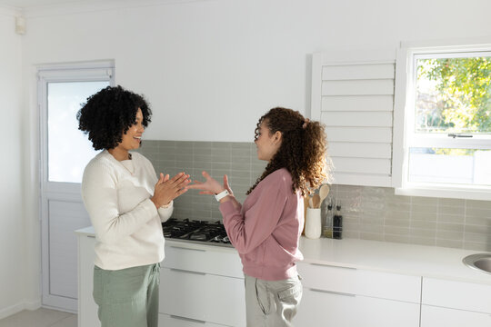 African American mom and teenage daughter chatting in home kitchen by gas cooktop with smartwatch