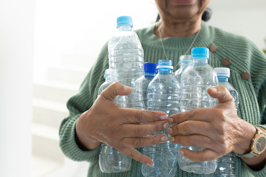 Senior African American woman holding empty water bottles with blue caps in hall in green sweater