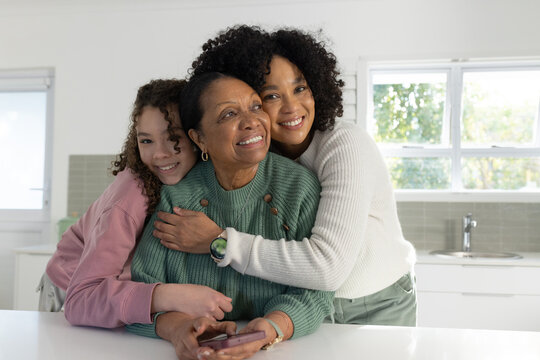 African American female family hugging at home counter senior holding smartphone adolescent leaning