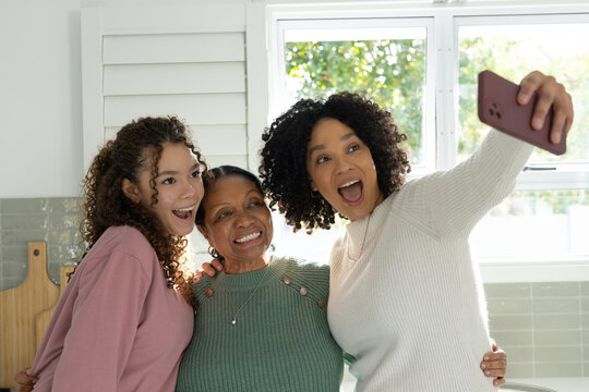 African American female family in green white pink taking selfie in kitchen with mauve smartphone