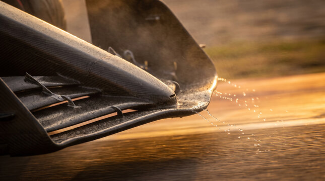 Racing car front wing close-up with water droplets at high speed.