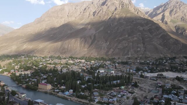 Aerial drone view of Khorog in the Pamirs, Tajikistan, with the city, a river and a large barren yellow-brown mountain