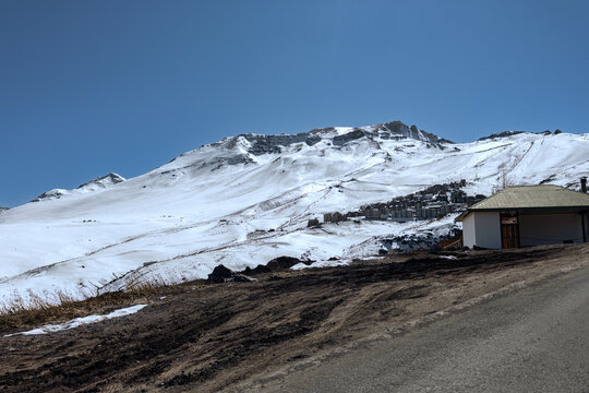 La parva ski resort village in the andes mountains, chile, under a clear blue sky, showing snow-covered slopes and rugged peaks contrasting with melting snow and dry terrain