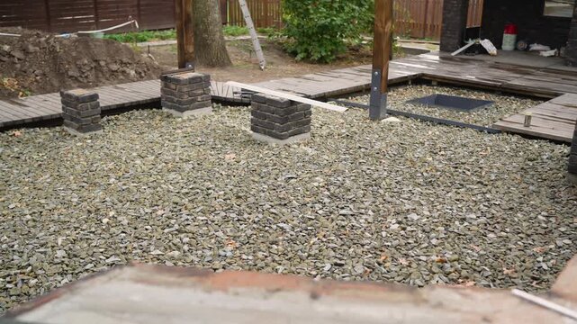 Unfinished patio or garden area during renovation. Shows installation of crushed stone, foundation work for pergola, and new walkways. Home improvement and DIY landscaping concept