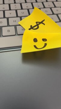 Yellow sticky note with dollar sign and smiley face on laptop keyboard
